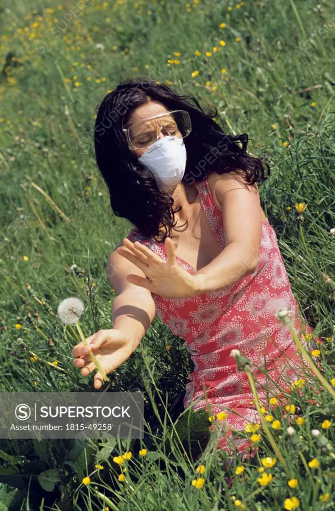 Woman wearing a mask and protective goggles sitting in a meadow, avoiding pollen