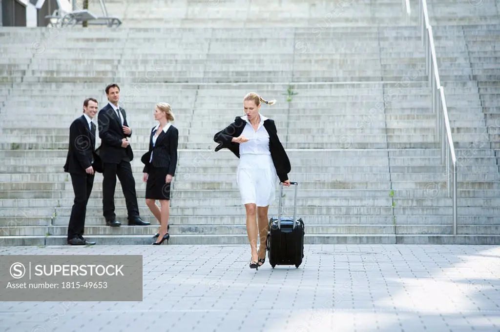 Germany, Baden_Württemberg, Stuttgart, Businesswoman walking with case, businesspeople in background