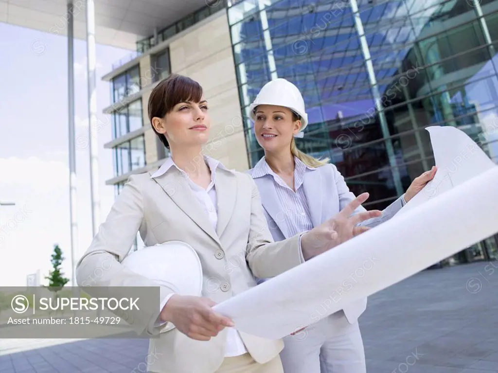Germany, Baden_Württemberg, Stuttgart, Two businesswomen with hard hats discussing building plan