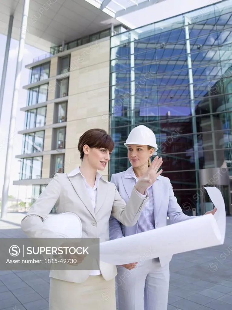 Germany, Baden_Württemberg, Stuttgart, two businesswomen with hard hats discussing building plan
