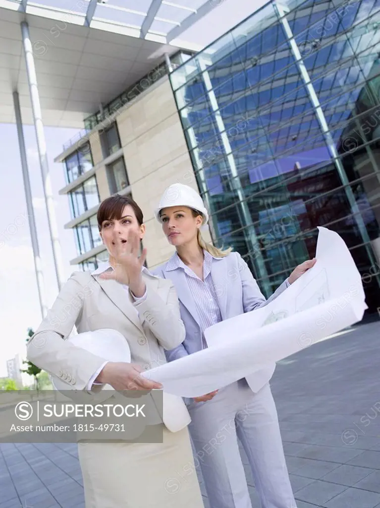 Germany, Baden_Württemberg, Stuttgart, two businesswomen with hard hats discussing building plan