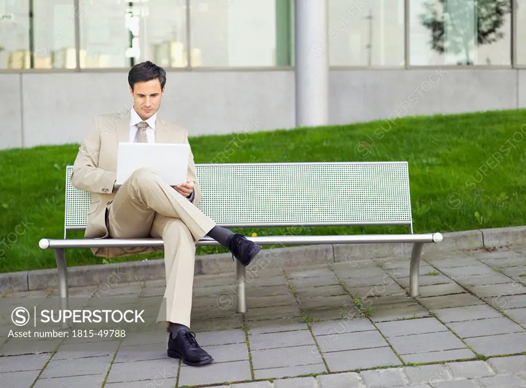 Germany, Baden_Württemberg, Stuttgart, Businessman on park bench using laptop