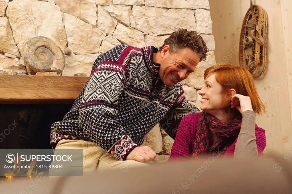 Couple sitting in living room by fireplace, smiling