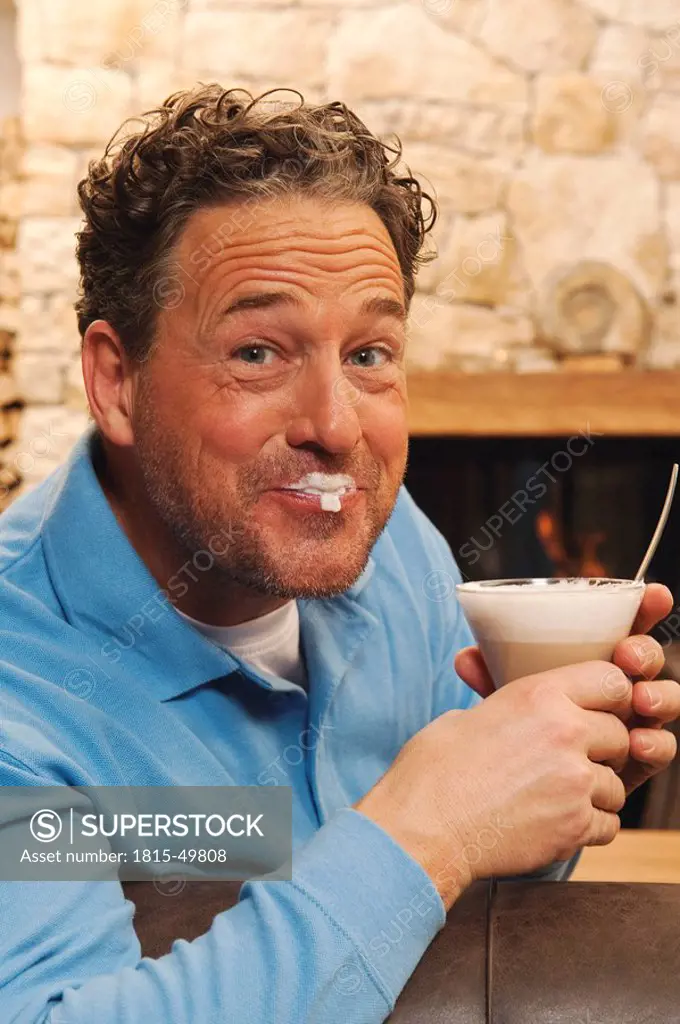 Man in living room holding glass of latte, smiling, portrait