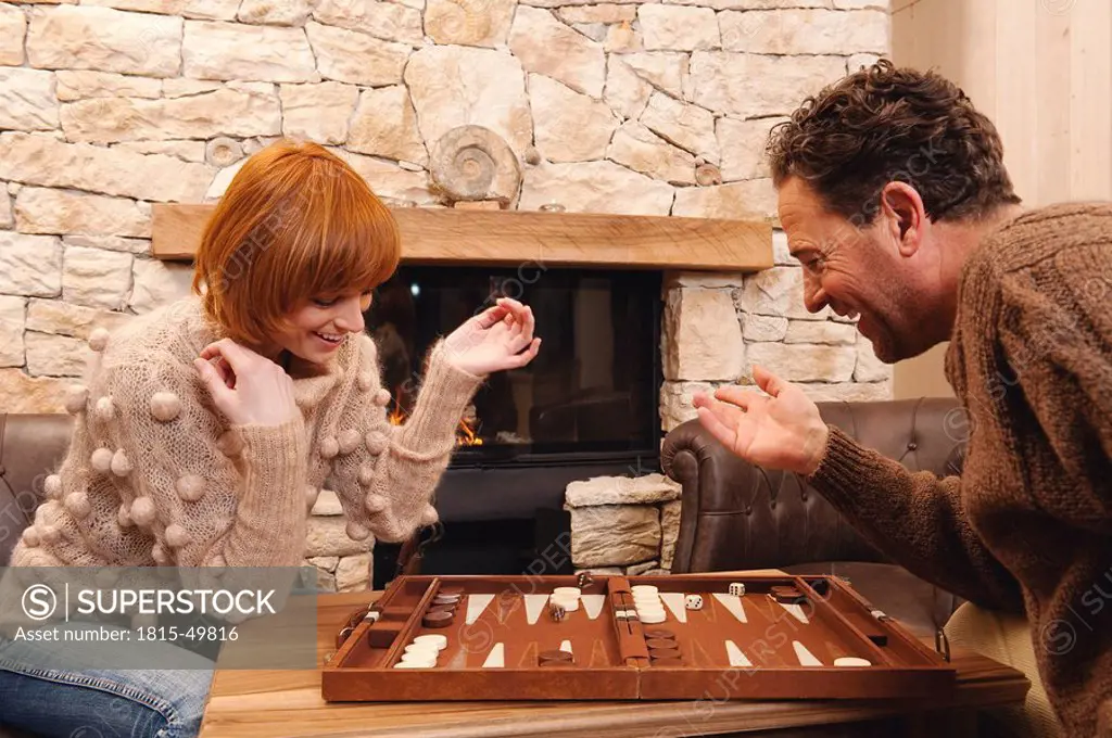 Couple playing backgammon, fireside in background