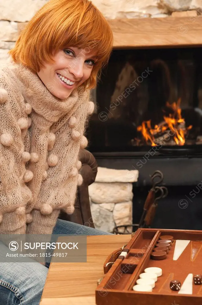 Woman sitting in front of fire place, smiling, backgammon board in foreground
