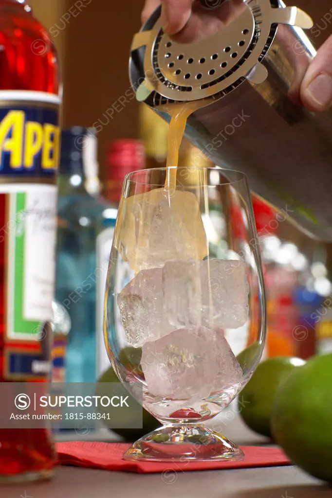Human hand pouring drink out of cocktail shaker into glass, close up.