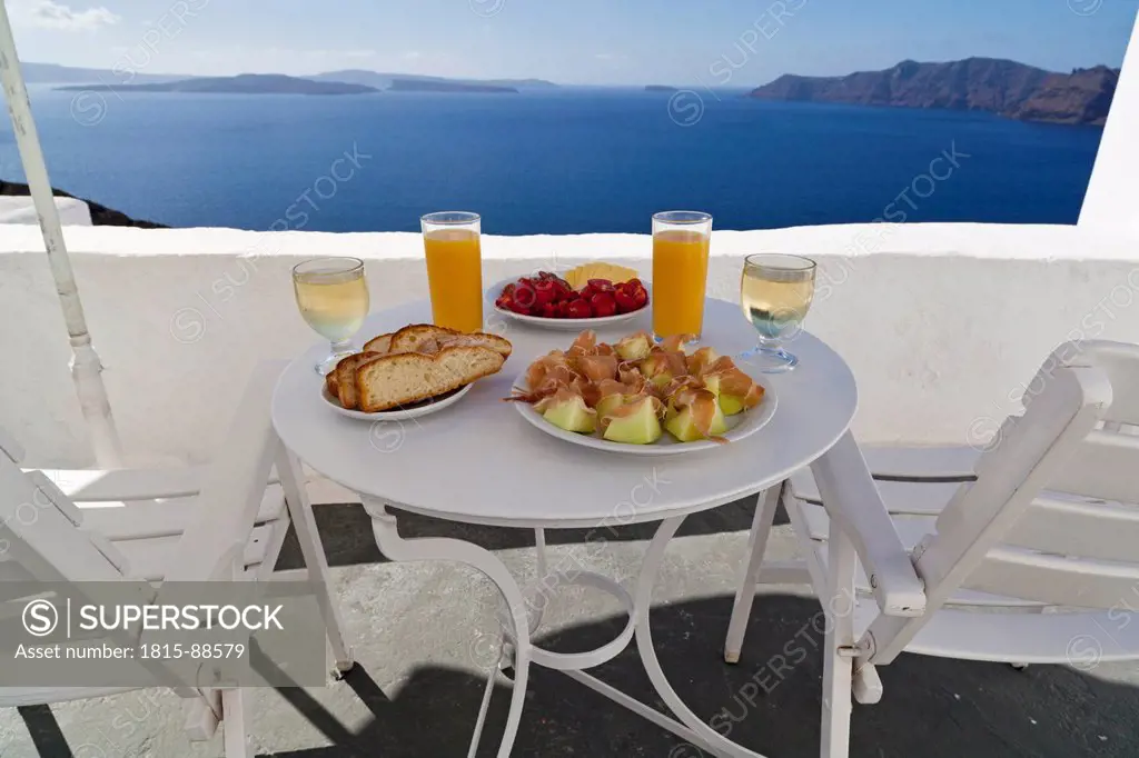 Greece, Cyclades,Thira, Santorini, Oia, Sunshade and furniture with food on terrace, blue sea in background