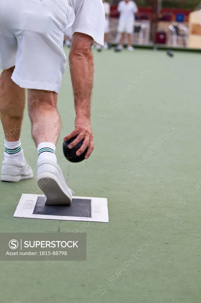 Spain, Denia, British senior man rolling bowling ball on bowling green