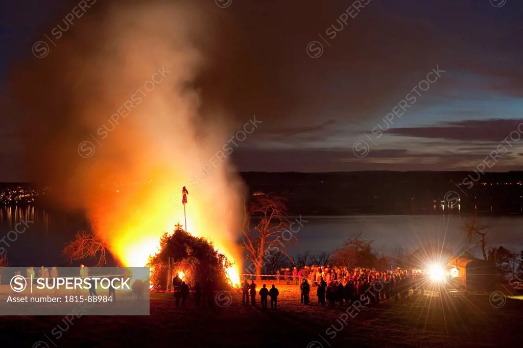 Germany, Nussdorf, Lake Constance, People standing by bonfire beside lake at night