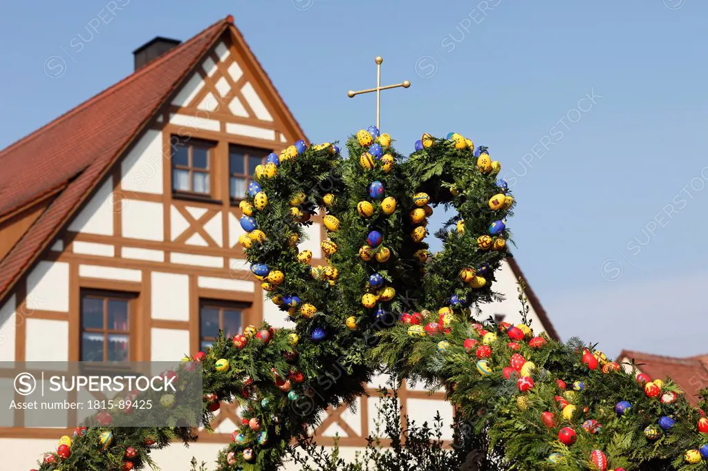 Germany, Bavaria, Franconia, Franconian Switzerland, Kirchehrenbach, View of decorated easter well with timber framed house in background