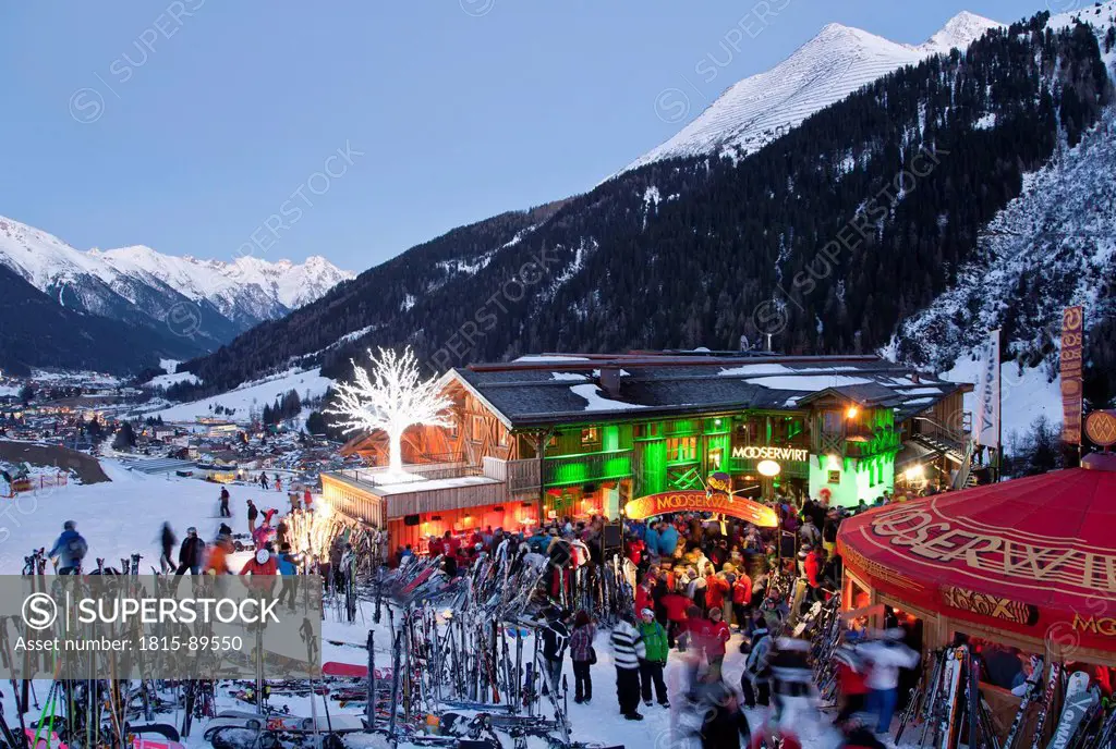 Austria, Tyrol, St. Anton am Arlberg, Mooserwirt, People skiing near ski hut in winter at dusk