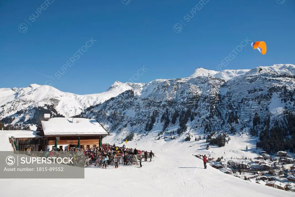 Austria, Vorarlberg, Lech am Arlberg, People skiing and paragliding near ski hut in winter