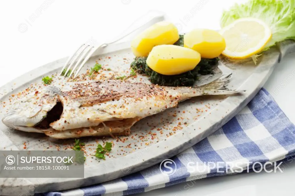 Garnished gilthead bream in plate with napkin on white background