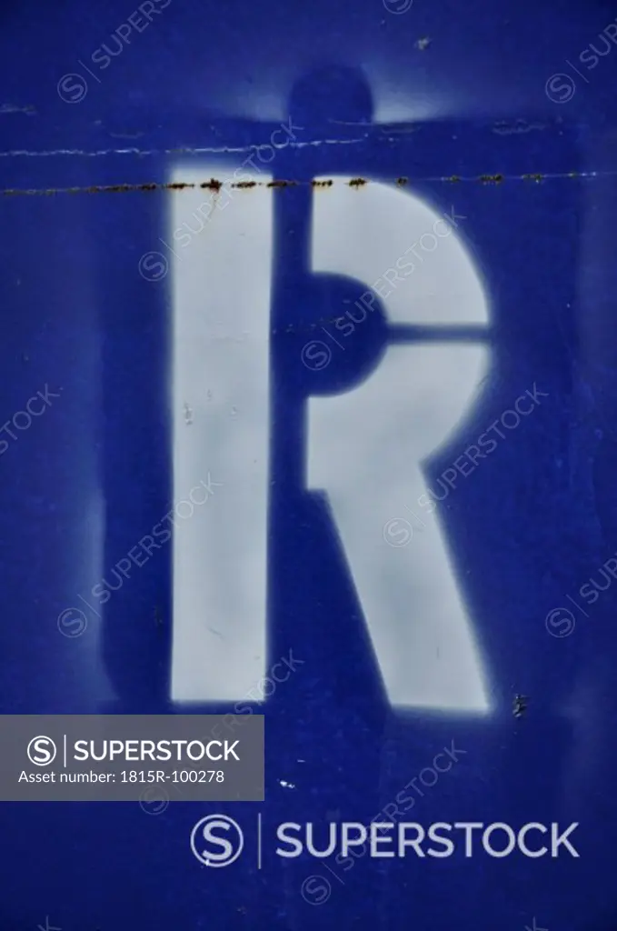 White spray paint letter R on blue, close up