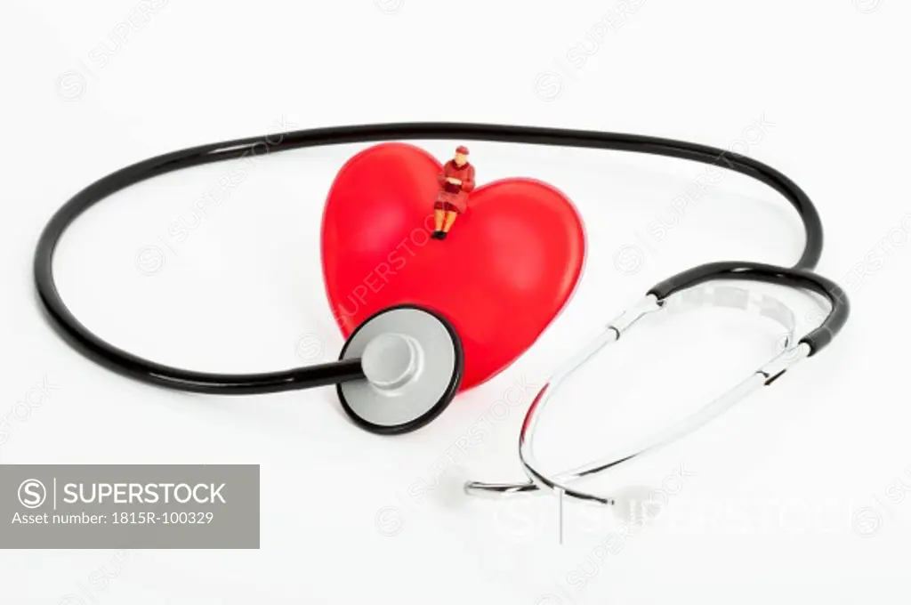 Figurine sitting on heart with stethoscope on white background