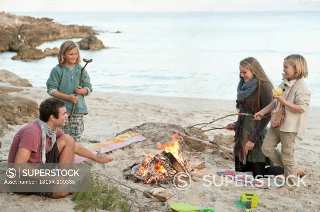 Spain, Mallorca, Friends grilling sausages at camp fire on beach