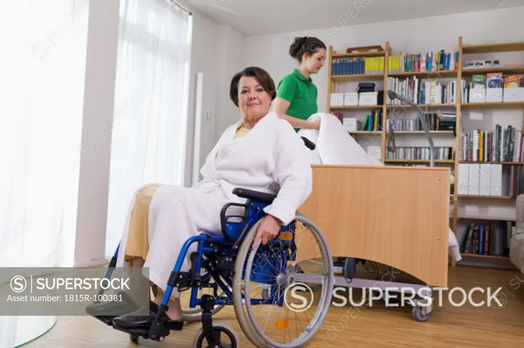 Germany, Leipzig, Senior woman sitting on wheelchair another woman arranging medical bed