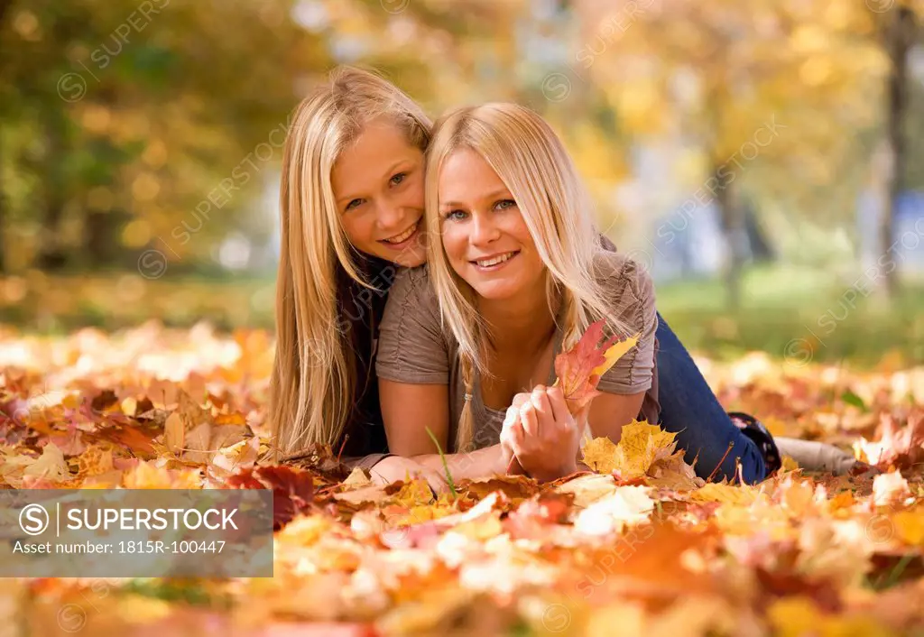 Austria, Sisters lying on autumn leaf, smiling, portrait