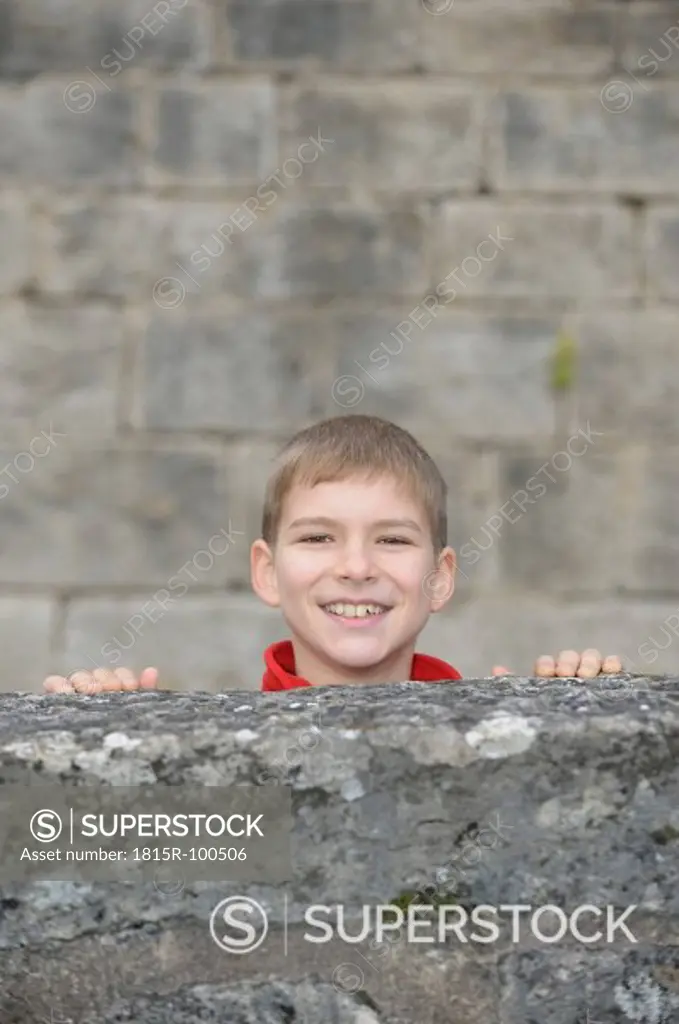Germany, Bavaria, Boy hiding behind wall, smiling, portrait
