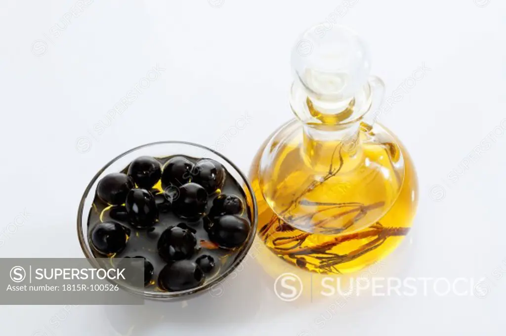 Black olives in glass bowl and bottle of olive oil on white background
