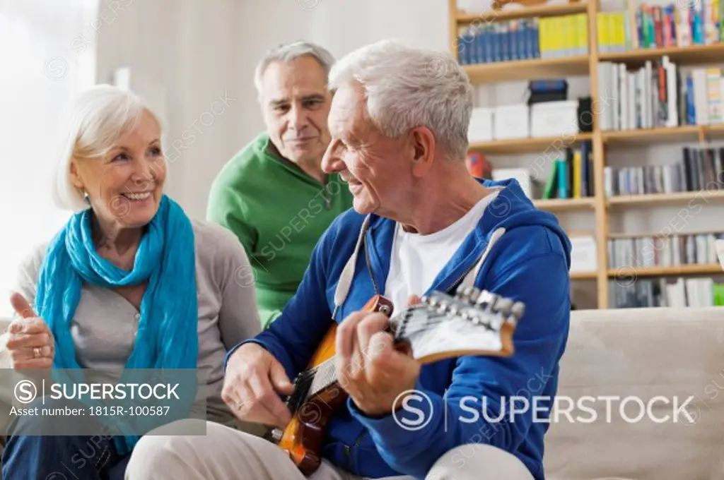 Germany, Leipzig, Senior man playing electric guitar, man and woman sitting besides