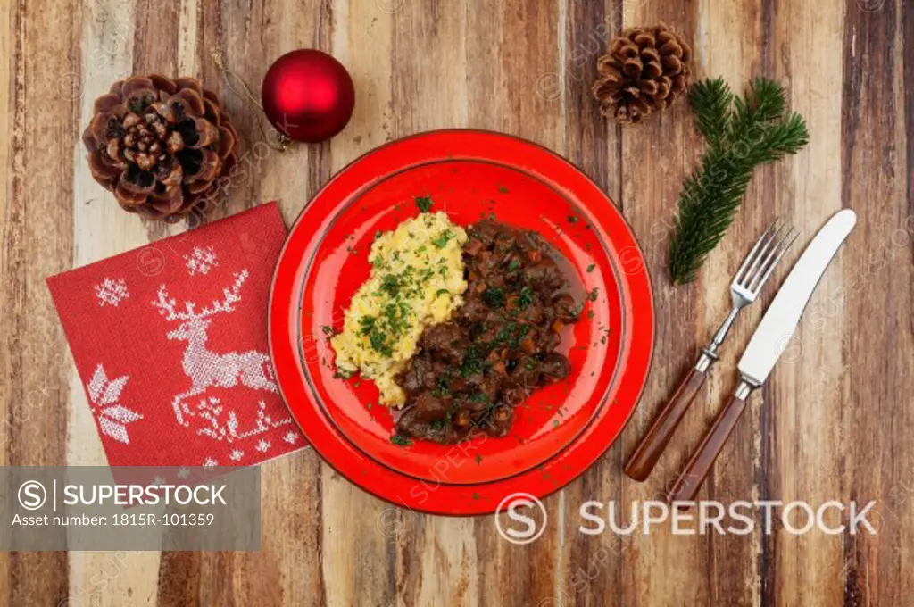 Plate of cooked venison goulash with mashed potatoes and Christmas decoration on wooden background