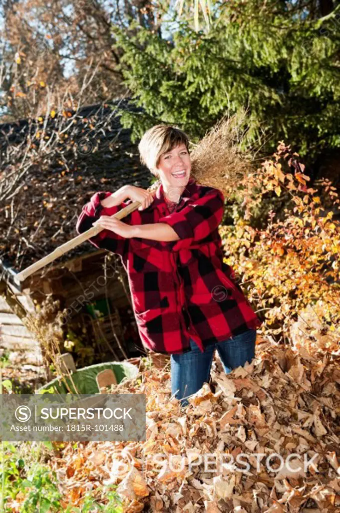 Austria, Salzburg County, Young woman standing in autumn leaves with broom on shoulder, smiling