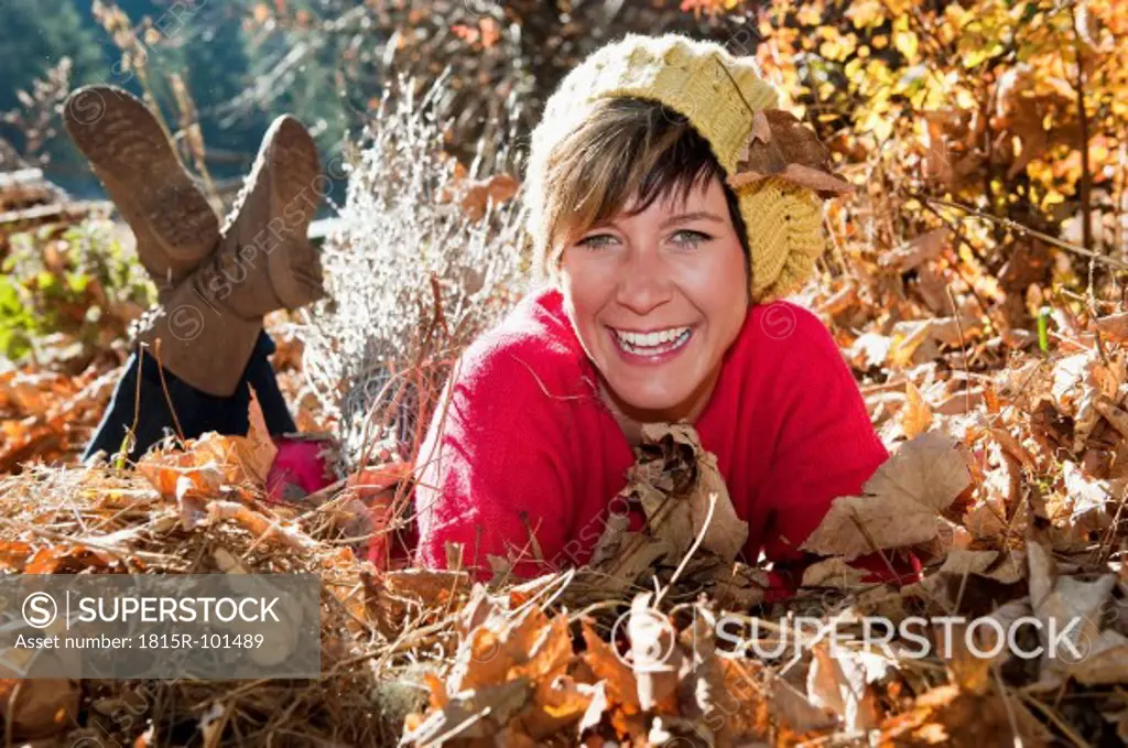 Austria, Salzburg County, Young woman lying on autumn leaves, smiling, portrait