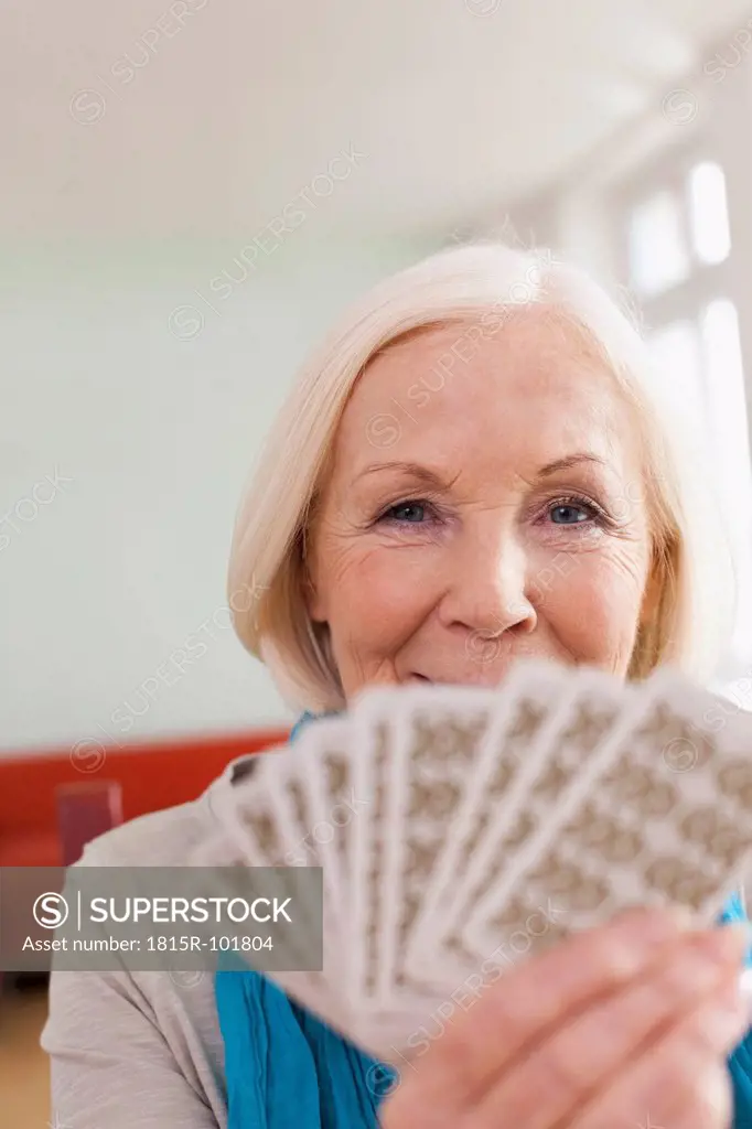 Germany, Leipzig, Senior woman playing cards, smiling, portrait