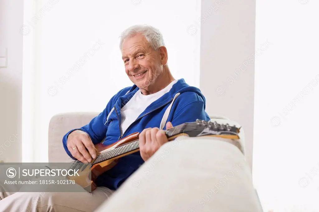 Germany, Leipzig, Senior man sitting on sofa and plucking guitar