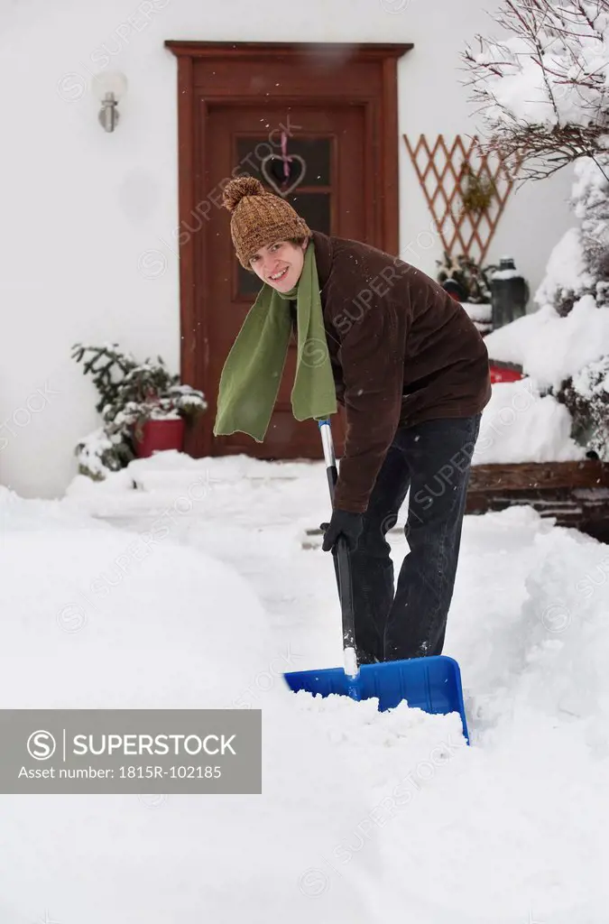 Austria, Young man shoveling snow in front of house, portrait