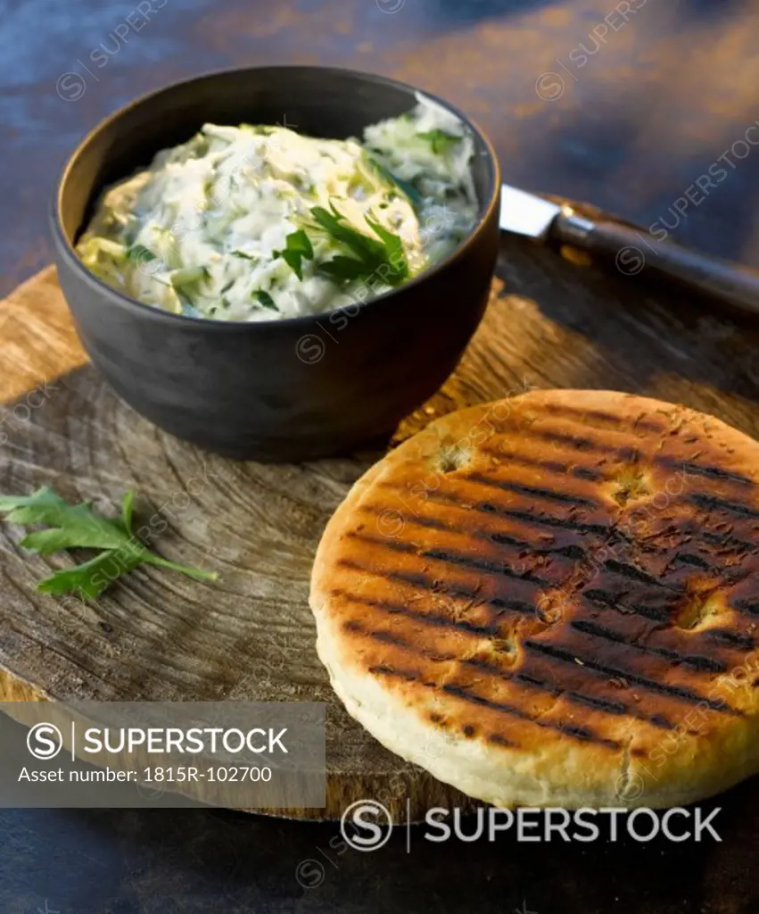 bowl of tzatziki with grilled bread on wooden board, close up