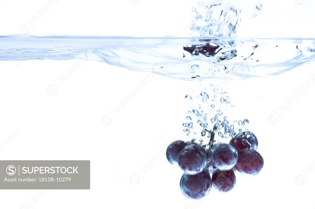 Red grapes splashing into water