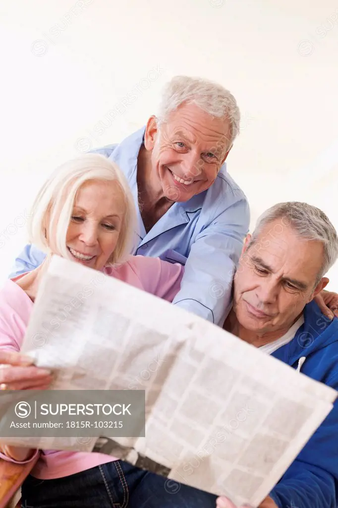 Germany, Leipzig, Senior men and woman reading newspaper, smiling
