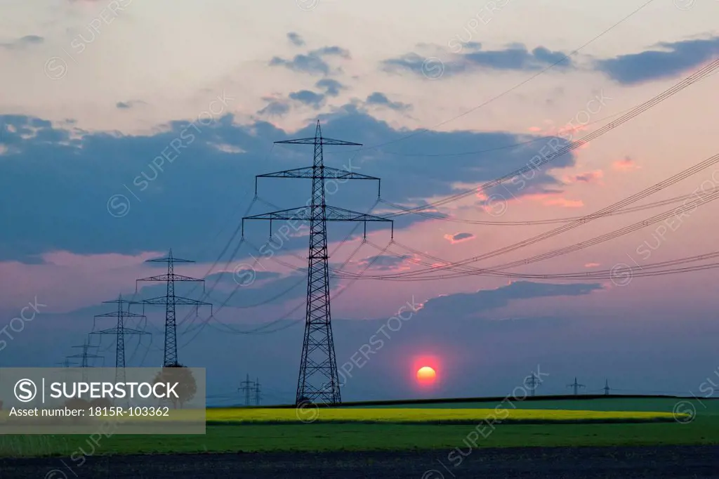 Germany, Bavaria, View of electricity pylon in rapeseed field at sunset