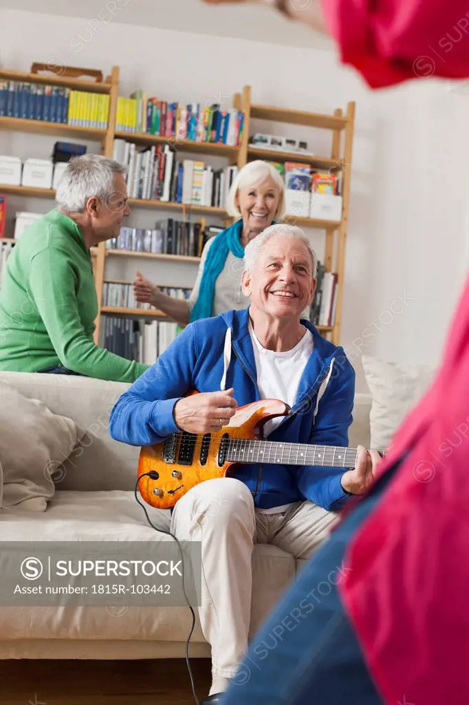 Germany, Leipzig, Senior man playing electric guitar, man and woman in background
