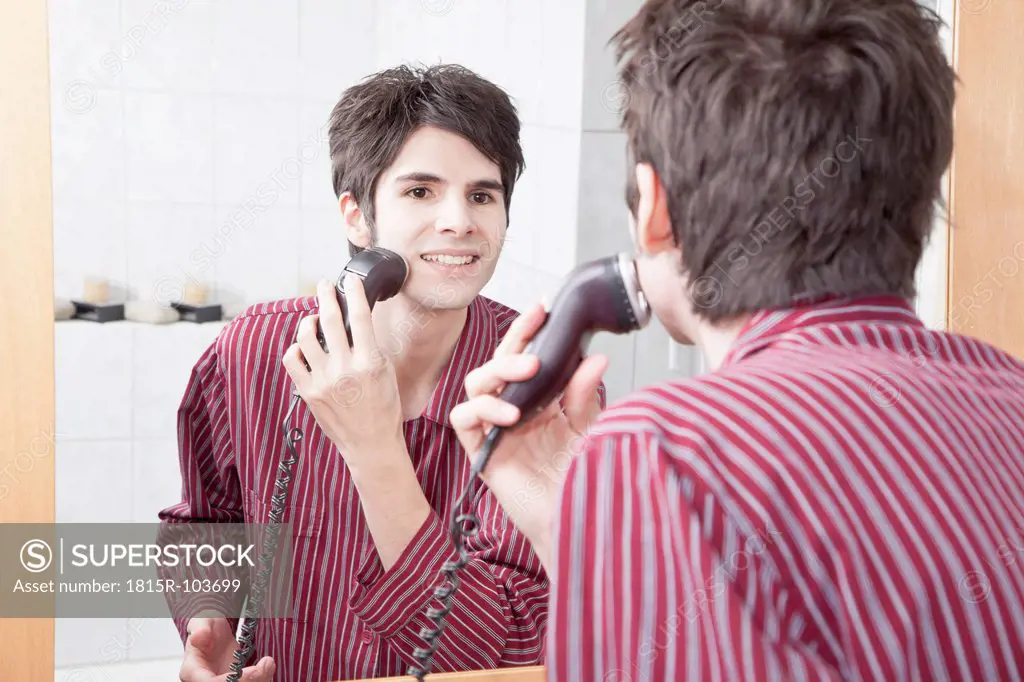 Young man doing shaving with electric razor