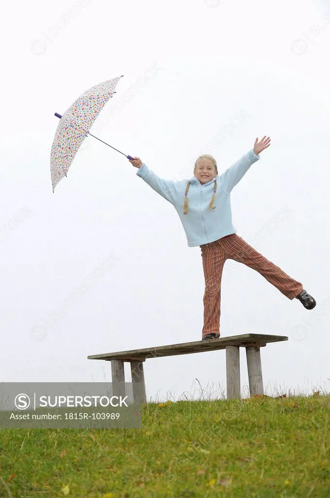 Germany, Bavaria, Girl standing on bench and holding umbrella, smiling