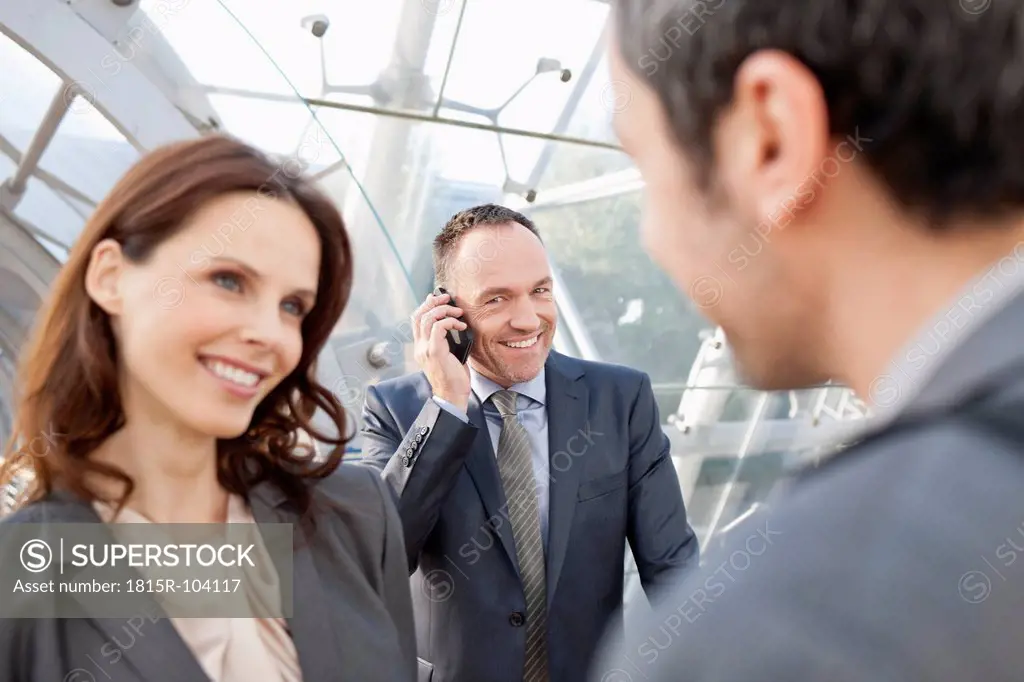Germany, Leipzig, Business people smiling, businessman with cell phone in background