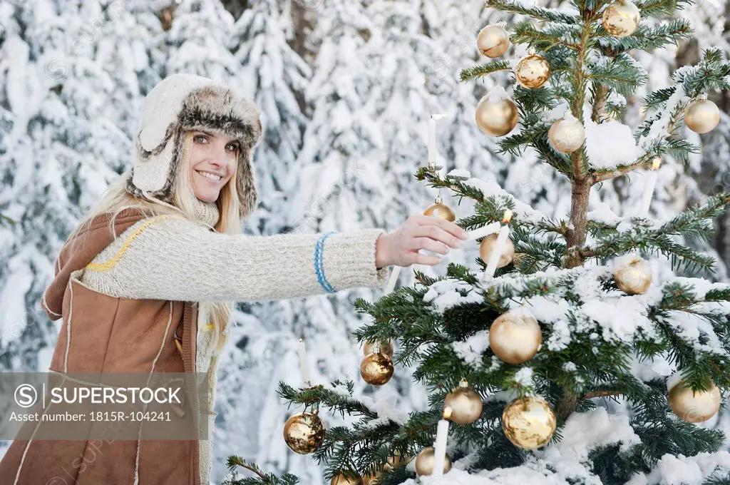 Austria, Salzburg County, Mid adult woman lighting candle on Christmas tree, smiling, portrait