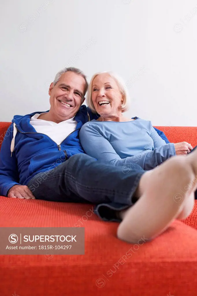Germany, Leipzig, Senior man and woman relaxing on couch, smiling