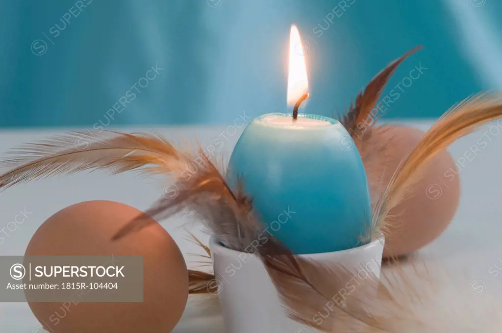 Egg shape candle in egg cup with egg and feather, close up