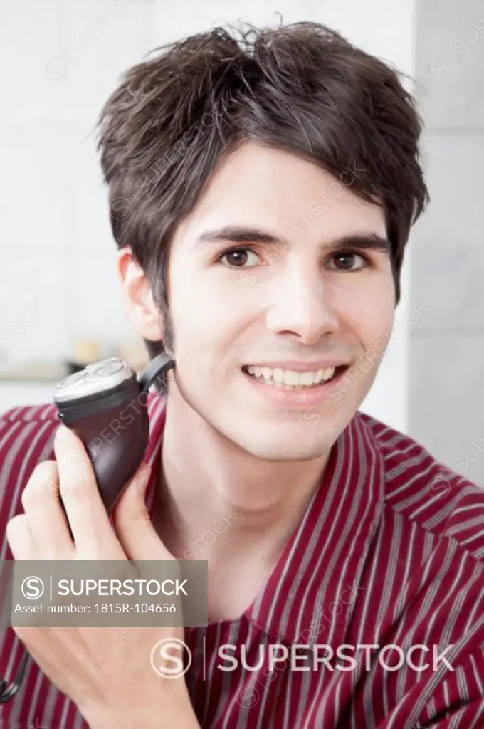 Young man doing shaving with electric razor, portrait