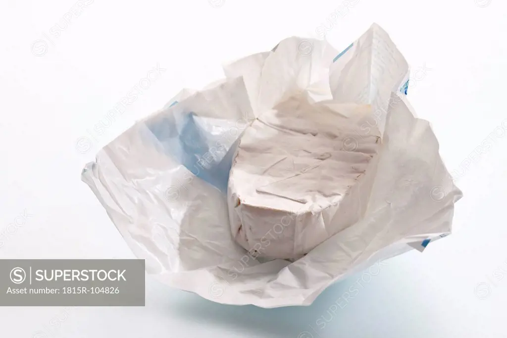 Piece of soft cheese in wax paper on white background