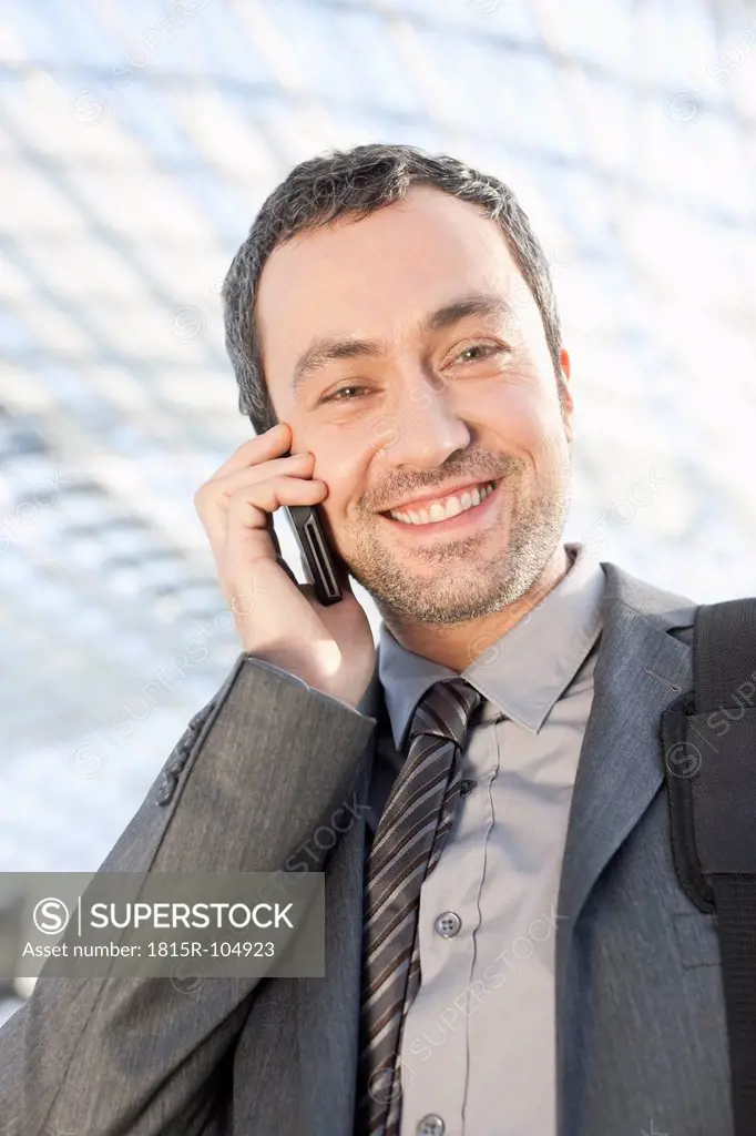 Germany, Leipzig, Businessman using cell phone, smiling, portrait