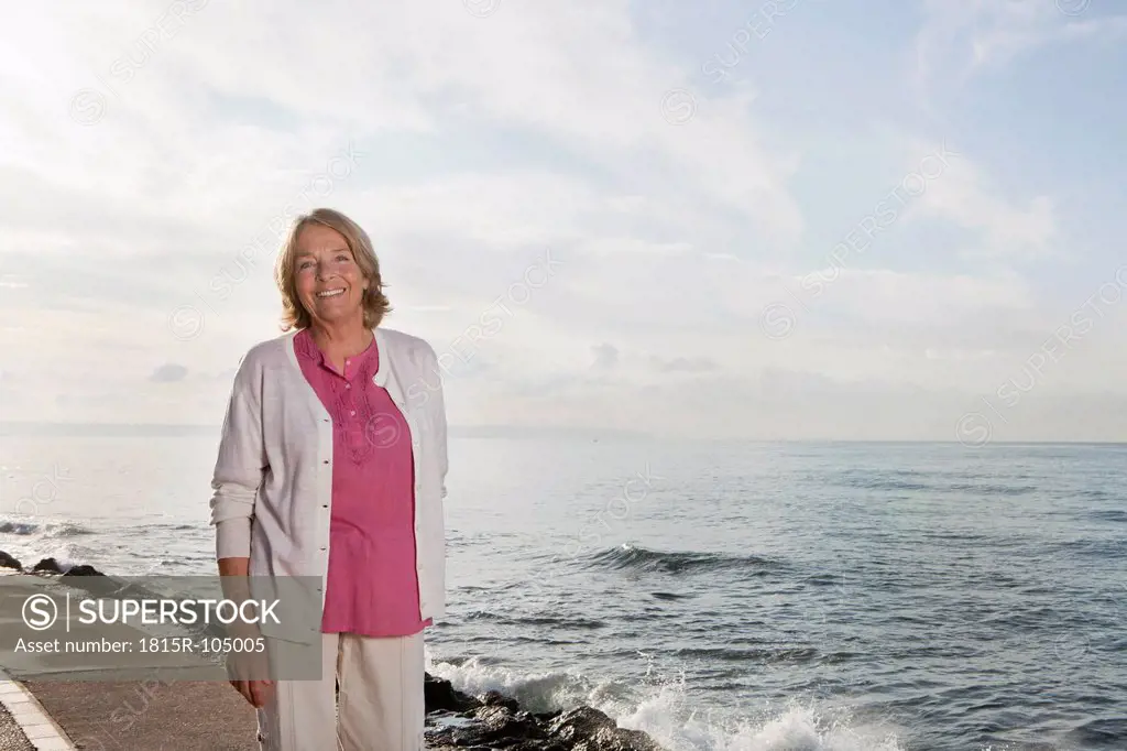 Spain, Mallorca, Senior woman standing at sea shore, smiling, portrait