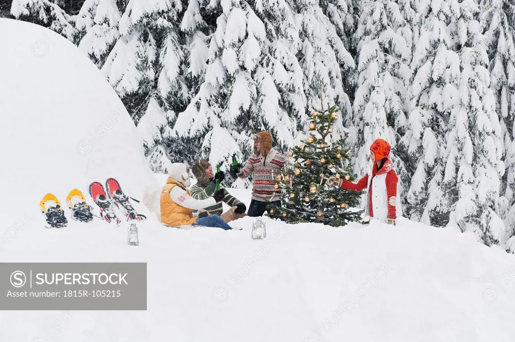 Austria, Salzburg, Men and women sitting by christmas tree in winter