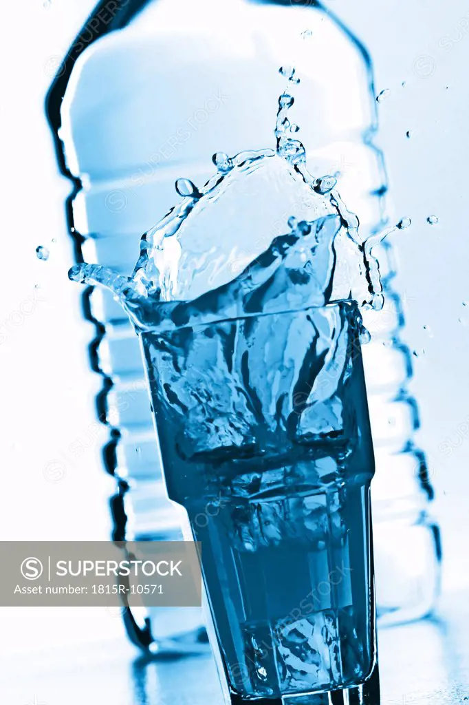 Splashing glas of water in front of a bottle