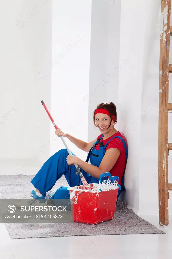 Germany, Bavaria, Young woman sitting with paint tin and paint brush, smiling, portrait